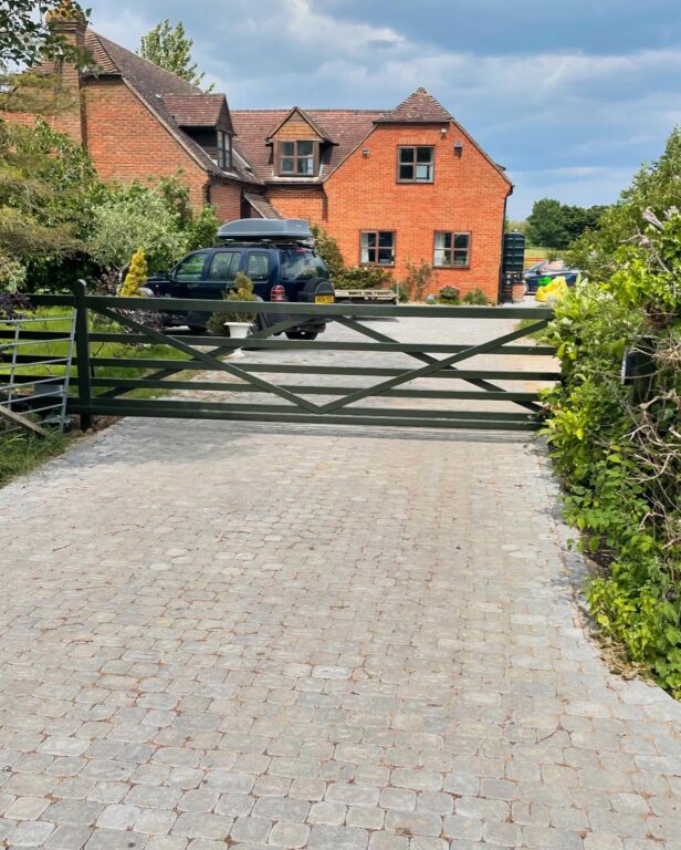 Black metal security gates across a gravel driveway leading to a rural house