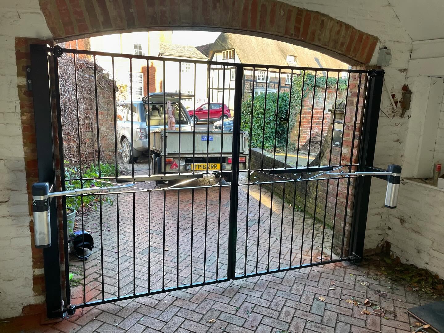 Black metal security gates with automatic openers beneath a brick archway