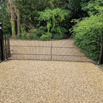Metal security gate between black posts at a tree-lined driveway