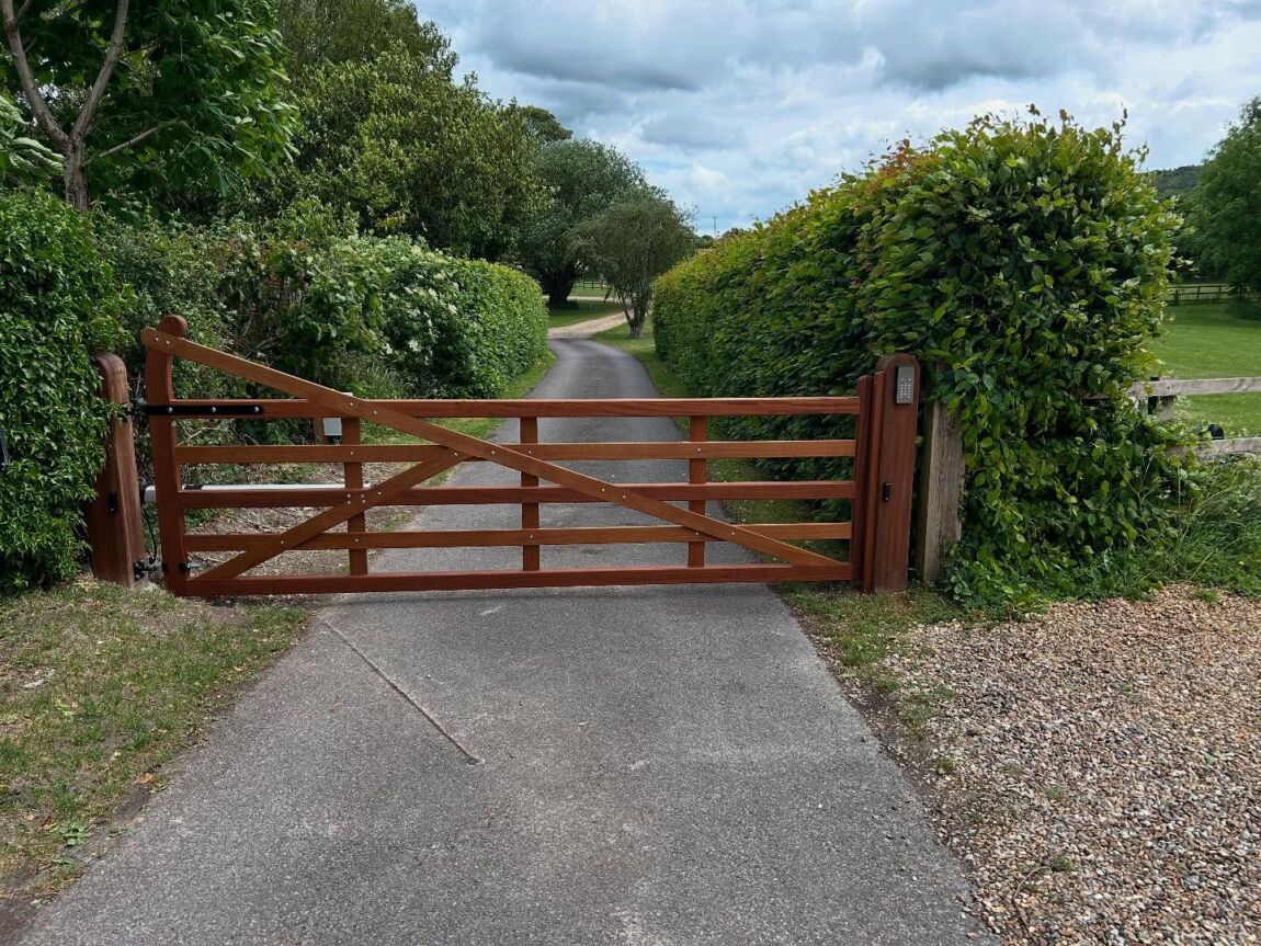 Wooden security gate across a hedge-lined rural driveway